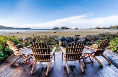 Empty chairs and tables at beach against sky