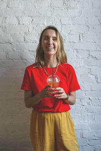 Portrait of a smiling young woman standing against wall