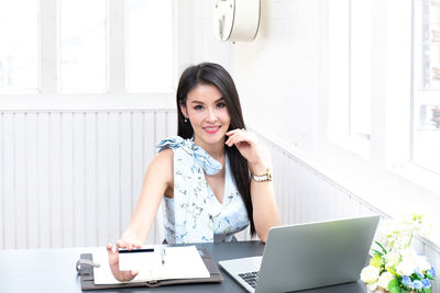 Portrait of young woman using phone while sitting on table