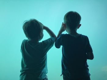 Rear view of boys standing against turquoise fish tank in aquarium