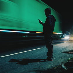 Man using phone by blurred motion of truck on road at night