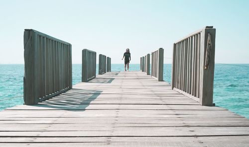 Rear view of man standing on pier at sea against sky