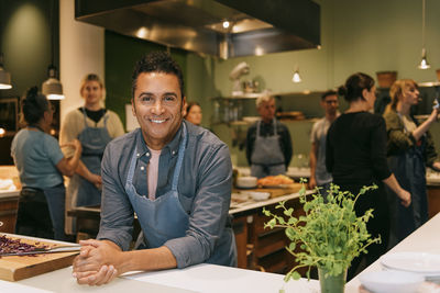 Portrait of confident male student leaning on kitchen counter during cooking class