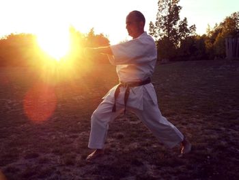 Mature man practicing karate while standing on field against sky during sunset