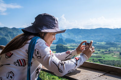 Portrait of young woman sitting on mountain against sky