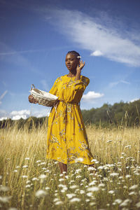 Young woman standing on field against sky