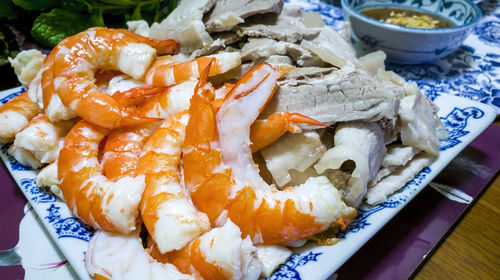 Cooked shrimps prawns in halves on a serving plate, along with thinly sliced boiled pork meat.