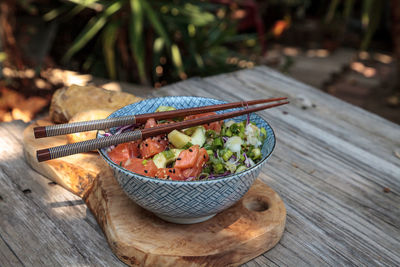 Raw salmon poke bowl with rice, cabbage, cucumber, sesame seeds and spring rolls with chopsticks.