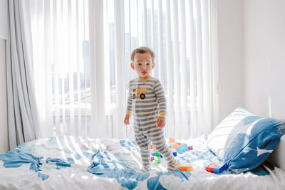 Boy toddler standing on bed in room at home and looking at camera. adorable innocent baby 