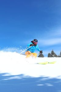 Man skiing on snow covered mountain against blue sky