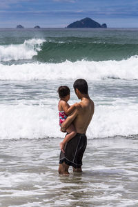 Rear view of shirtless father carrying daughter in sea
