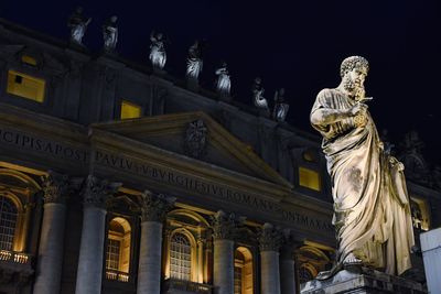 Low angle view of statue against st peters basilica in city at night