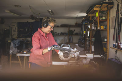 Senior woman using circular saw in workshop