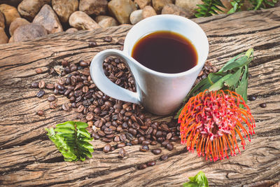 High angle view of coffee cup with flower and roasted beans on wood