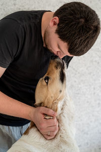 Man kissing dog outdoors against wall