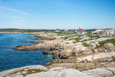 Scenic view of peggy's cove rocky shore against blue sky.
