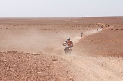 People riding motorcycle on desert against clear sky