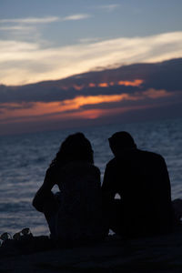 Rear view of silhouette friends on shore against sunset sky