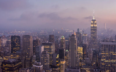 Illuminated buildings in city against cloudy sky