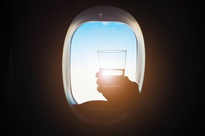 Cropped hand holding glass of water by airplane window