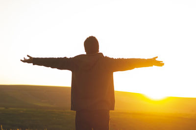 Rear view of man with arms outstretched against sky during sunset