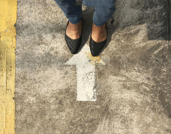 Low section of woman standing by arrow sign on road