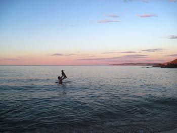 View of father and son enjoying in sea against sky during sunset