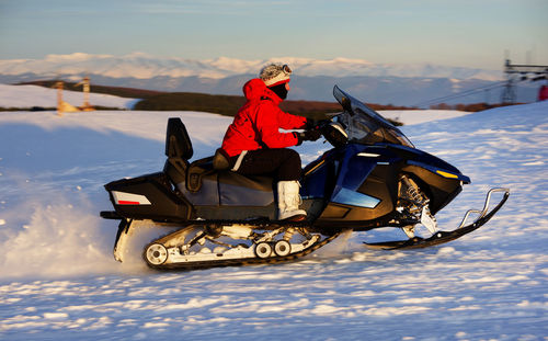 Side view of man riding snowmobile on snow covered landscape