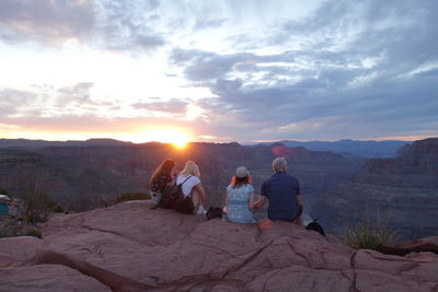 People sitting on rock against sky during sunset
