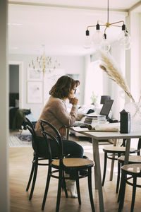 Woman sitting at table at home talking to coworkers in online meeting