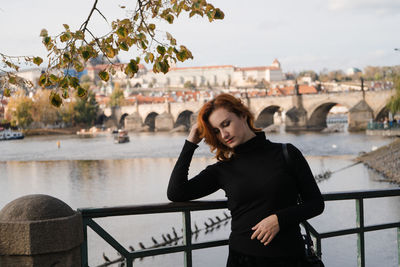 Young woman using phone while standing on railing against bridge