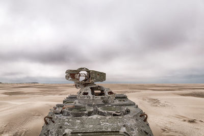 Abandoned armored tank at desert against cloudy sky