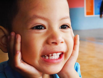 Close-up of smiling boy with hands on chin looking away