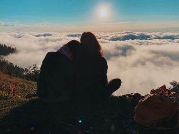 Rear view of people sitting against sky during sunset
