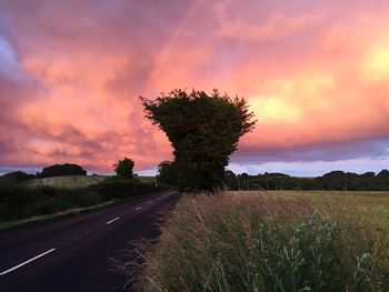 Road passing through field against cloudy sky