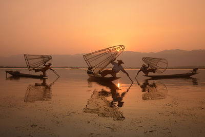 Fishermen fishing in lake against sky during sunset