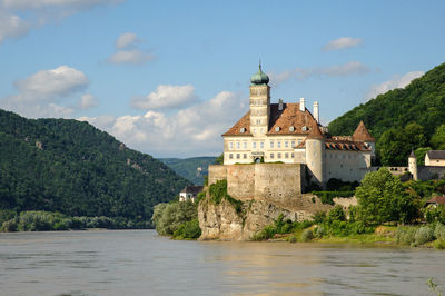 View of building by river against cloudy sky