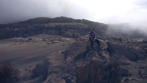 Man standing on rock against sky