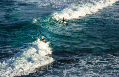 High angle view of people surfboarding on waves in sea