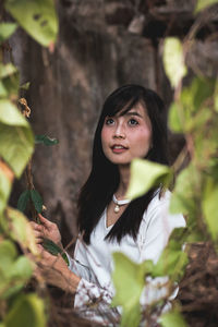 Young woman holding plant while looking away in forest