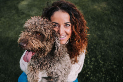 High angle portrait of smiling woman holding dog on grassy land