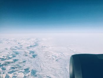 Close-up of airplane wing over sea against clear blue sky