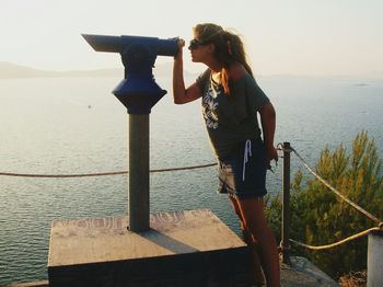 Woman looking through coin-operated binoculars against sea