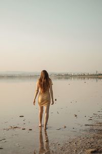 Rear view of woman standing on beach against sky