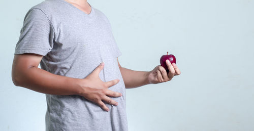 Midsection of man holding apple while standing against white background