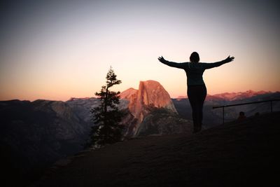 Rear view of woman with arms outstretched standing on mountain during sunset