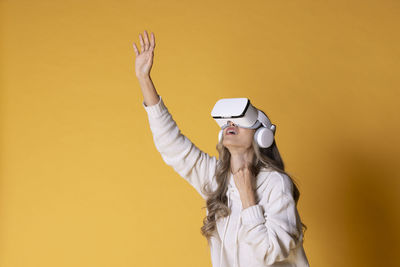 Young woman with arms raised standing against yellow wall