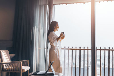 Side view of woman looking through window at hotel room