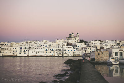 Buildings by sea against clear sky at sunset