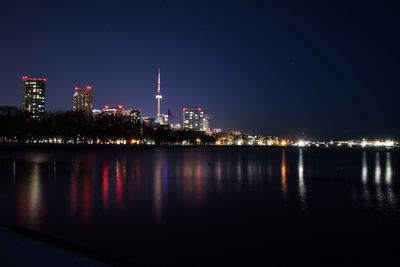 Illuminated buildings by river against sky at night